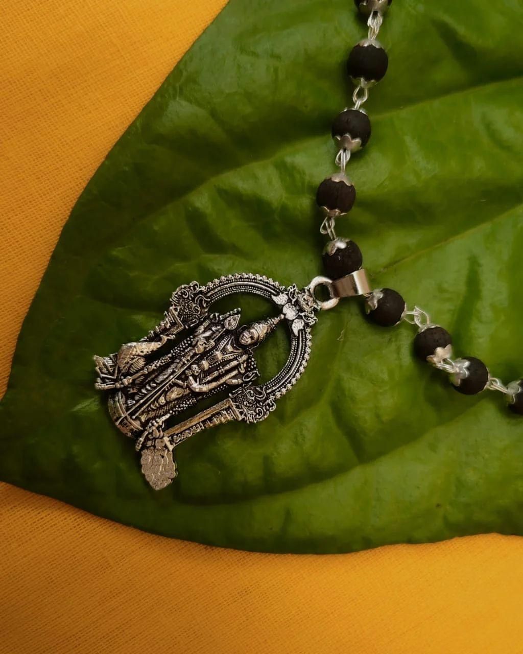 Karungali mala with silver Murugan locket on green leaf, showcasing traditional spiritual black beads.