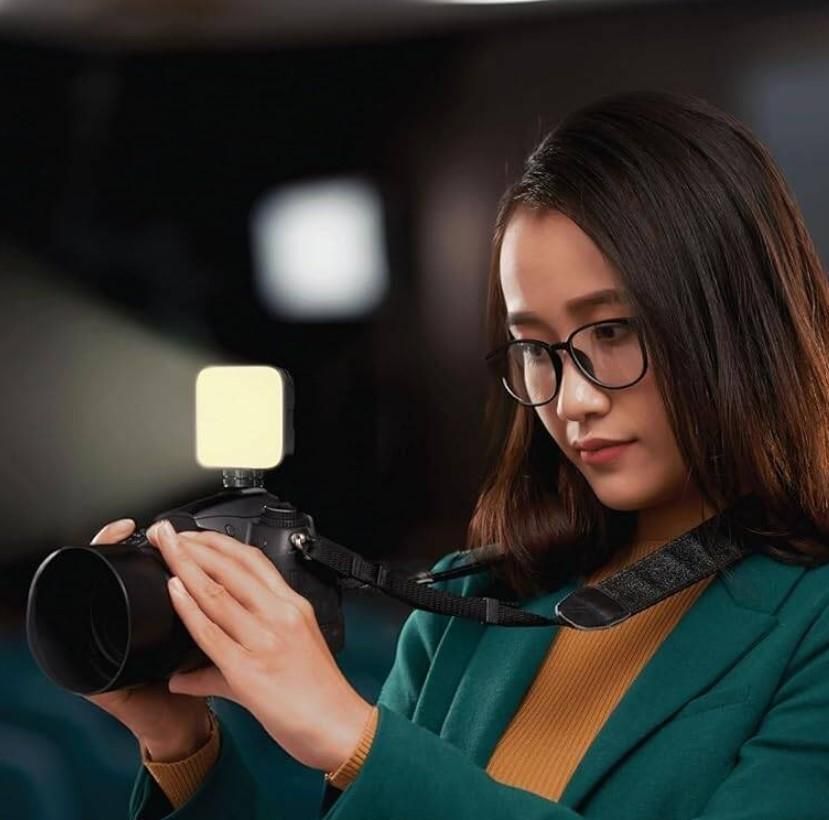 Woman holding a camera with aLED Video Light
 attachment in a blurred indoor setting