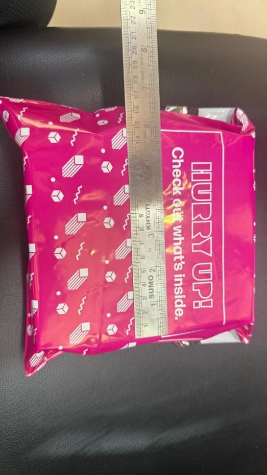Pink package with text and a ruler for scale on a dark surface