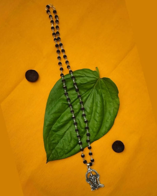 Karungali Mala with silver Murugan locket on green leaf, showcasing traditional black beads chain for men.