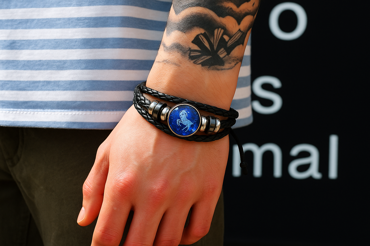 Person wearing a black leather bracelet with a blue emblem on a striped shirt sleeve.